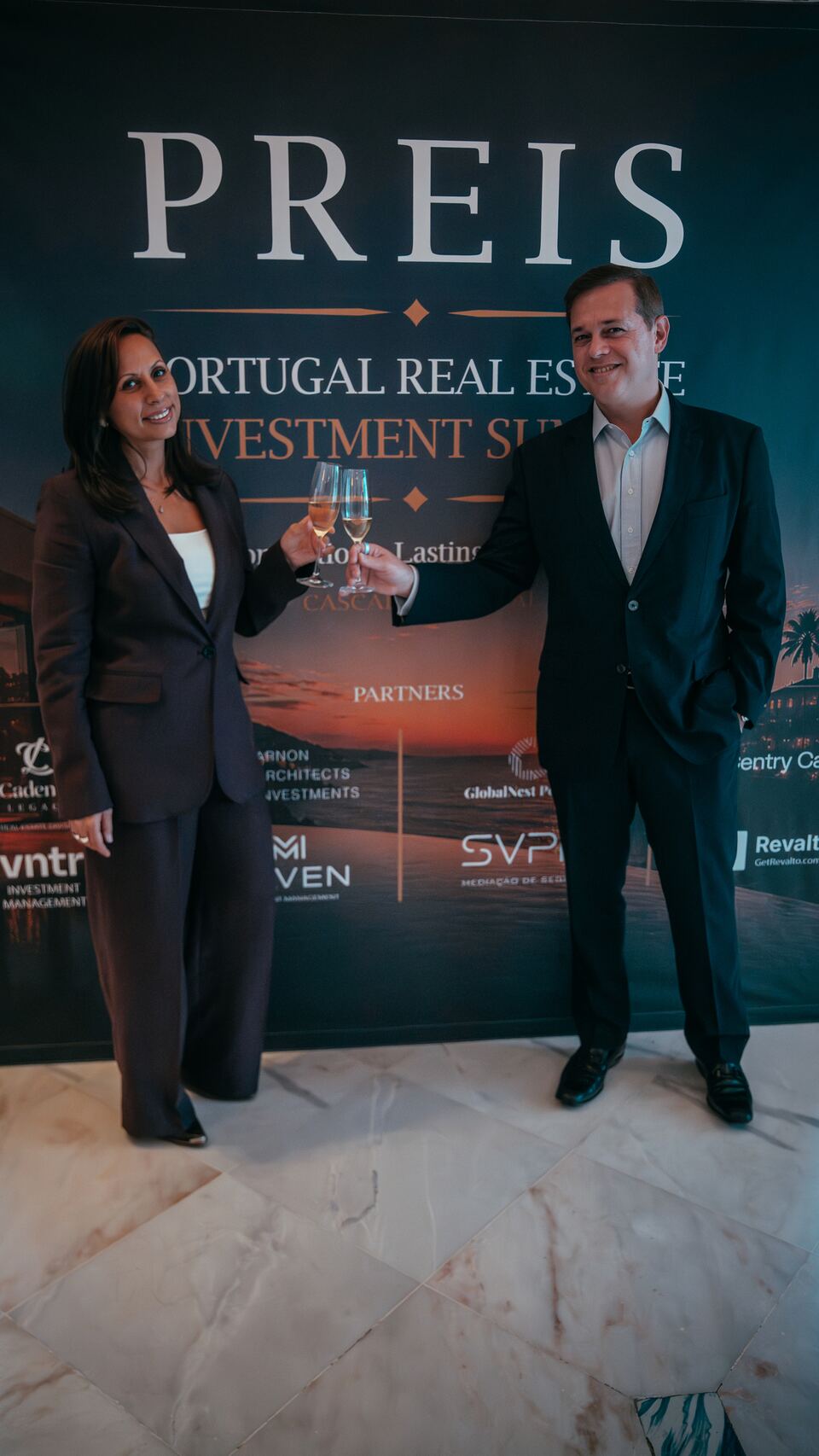 Two guests standing together in front of the PREIS summit backdrop